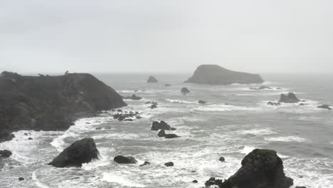 Aerial-circling-view-over-rough-ocean-and-waves-crashing-on-cliffs-near-Brookings,-USA