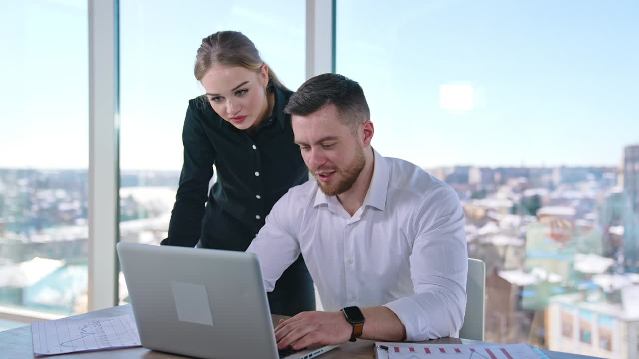 Young business people working in office. Handsome businessman listens to professional female advisor in office. Beautiful business woman and man discuss data on a laptop.