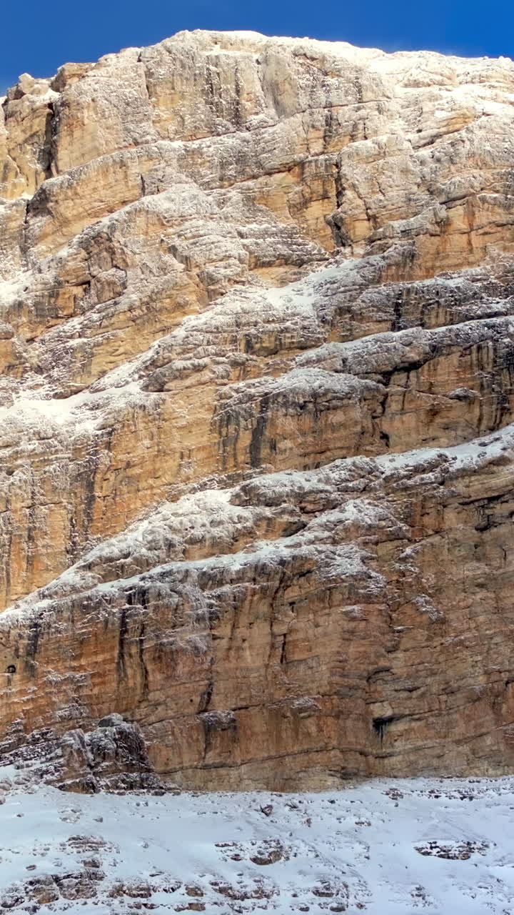 Aerial drone view of snow on the Sassongher mountain in the Dolomites, Italy with the blue sky on the background. Vertical