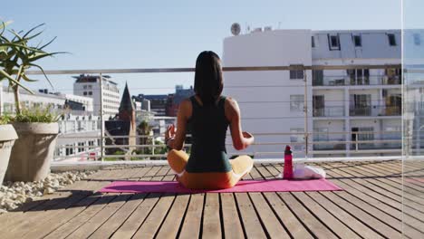 Mixed-race-gender-fluid-person-practicing-yoga-meditation-on-roof-terrace