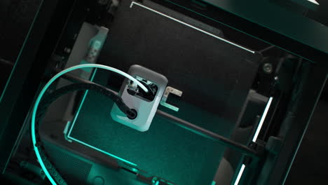 process of printing 3d object inside the 3d printer illuminated by blue light - table top view, dolly out
