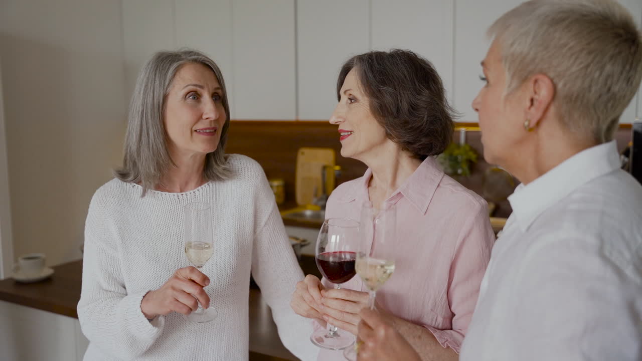 Grupo de amigas idosas alegres conversando e bebendo vinho na cozinha