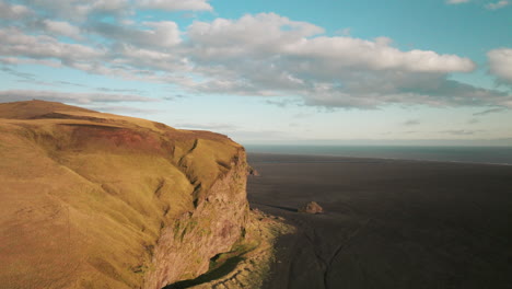 Sunlight-illuminating-golden-cliff-above-black-beach-in-Iceland