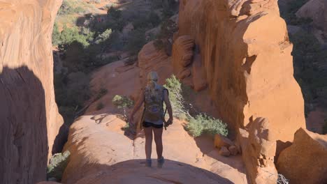 young blonde female hiking down a smooth rock formation in arches national park, utah