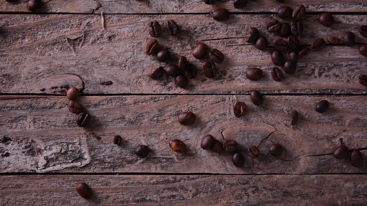 Chicchi di caffè tostati che cadono su una superficie di legno rustica