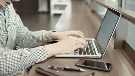 joven hombre de negocios asiático usando computadora portátil en el espacio de trabajo con teléfono inteligente y portátil en un escritorio de madera. mano masculina escribiendo en el teclado del portátil. estilo de vida independiente en el concepto de la era digital.