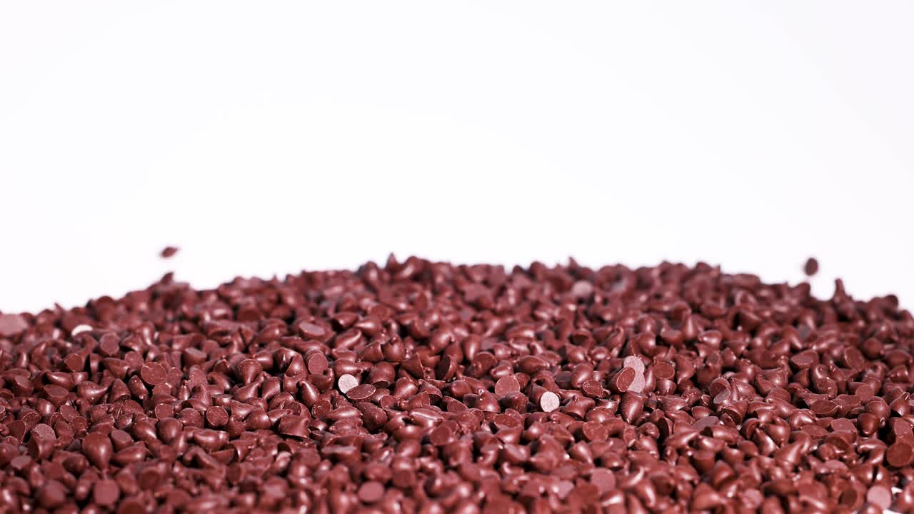 Chocolate drops cascade onto a pile, creating a dynamic and rich texture against a white background in slow motion