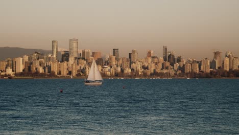 sail boat sailing on the jericho beach with skyscrapers of vancouver in the background in canada at dusk. - wide shot
