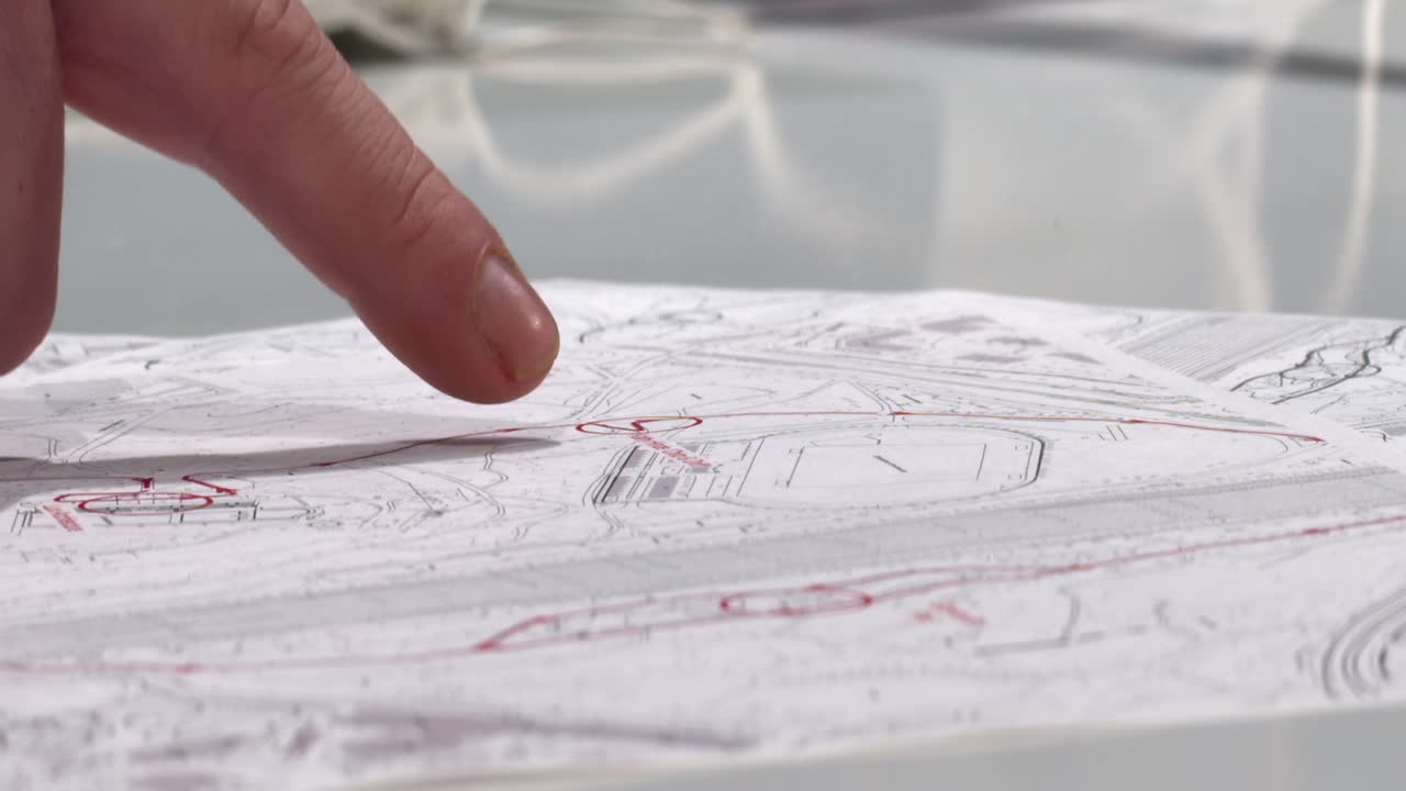 남자의 손가락은 탁자 위에 있는 청사진 세트의 세 점을 가리킨다