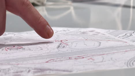 Man's finger points to three points on set of blueprints on table top