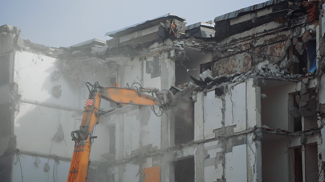 A scoop of demolishing machine breaks off the floors of the destroyed house. Excavator working in the cloud of dust .