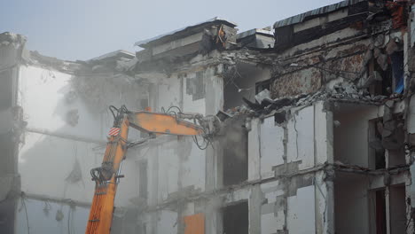 a scoop of demolishing machine breaks off the floors of the destroyed house. excavator working in the cloud of dust .