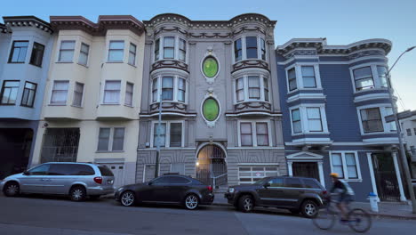 Frente-A-La-Casa-Victoriana-De-San-Francisco-Con-Extrañas-Ventanas-Verdes,-Scooters,-Bicicletas-Y-Autos-Pasan