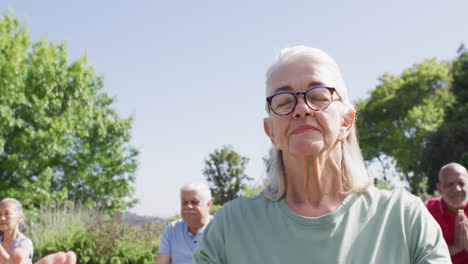 Ältere-Kaukasische-Frau-Praktiziert-Yoga-Meditation-Mit-Vielfältiger-Seniorengruppe-Im-Garten,-Zeitlupe