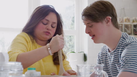 young downs syndrome couple mixing ingredients for cake recipe they are baking in kitchen at home