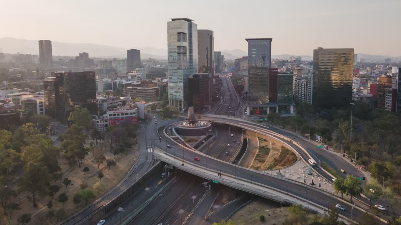 Drone hyperlapse moving right to left over Fuente de Petroleos roundabout and skyline in Mexico City at sunset