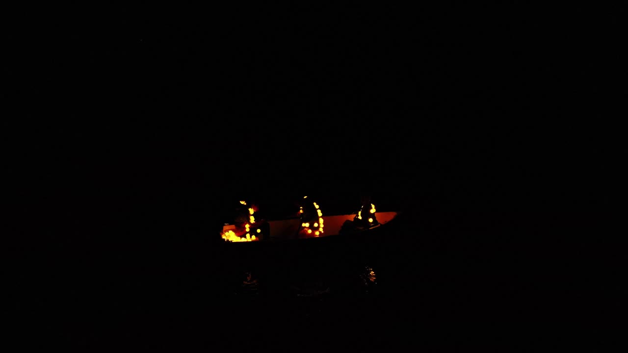 People With Garland Lights Riding And Paddling In The Lake On A Dark Night, - wide shot