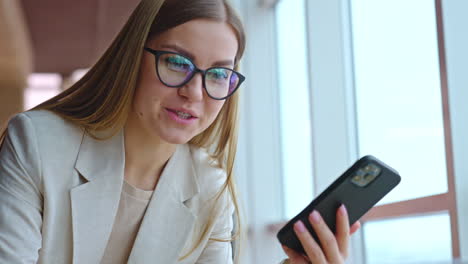 smiley young woman speaks on the phone cheerfully. long-haired woman in glasses bent over the screen. close up.