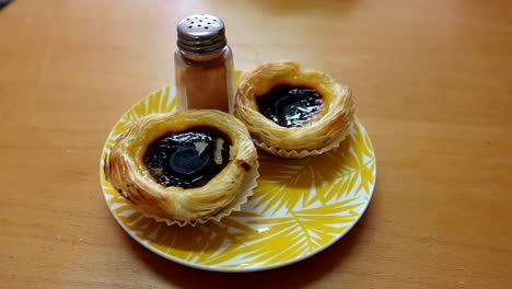 close up of pasteis de nata with cinnamon pot served in beautiful yellow plate