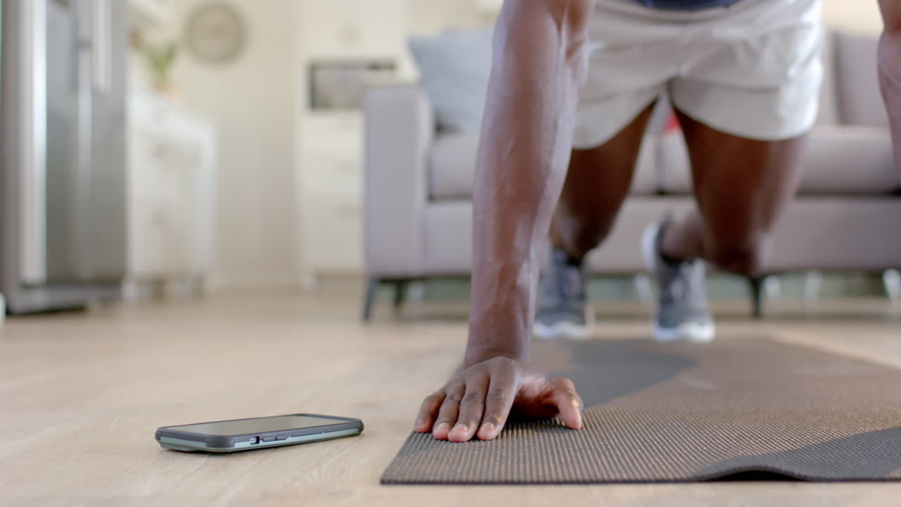 African american man doing mountain climbers using smartphone in living room, slow motion