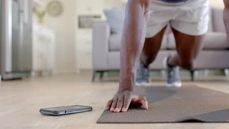 african american man doing mountain climbers using smartphone in living room, slow motion