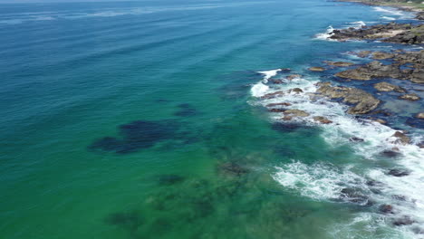 aerial shot looking at the clear turquoise sea crashing against the rocks on the west coast of scotland