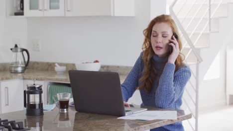 Mujer-Usando-Una-Computadora-Portátil-Mientras-Habla-Por-Teléfono-Inteligente-En-Casa