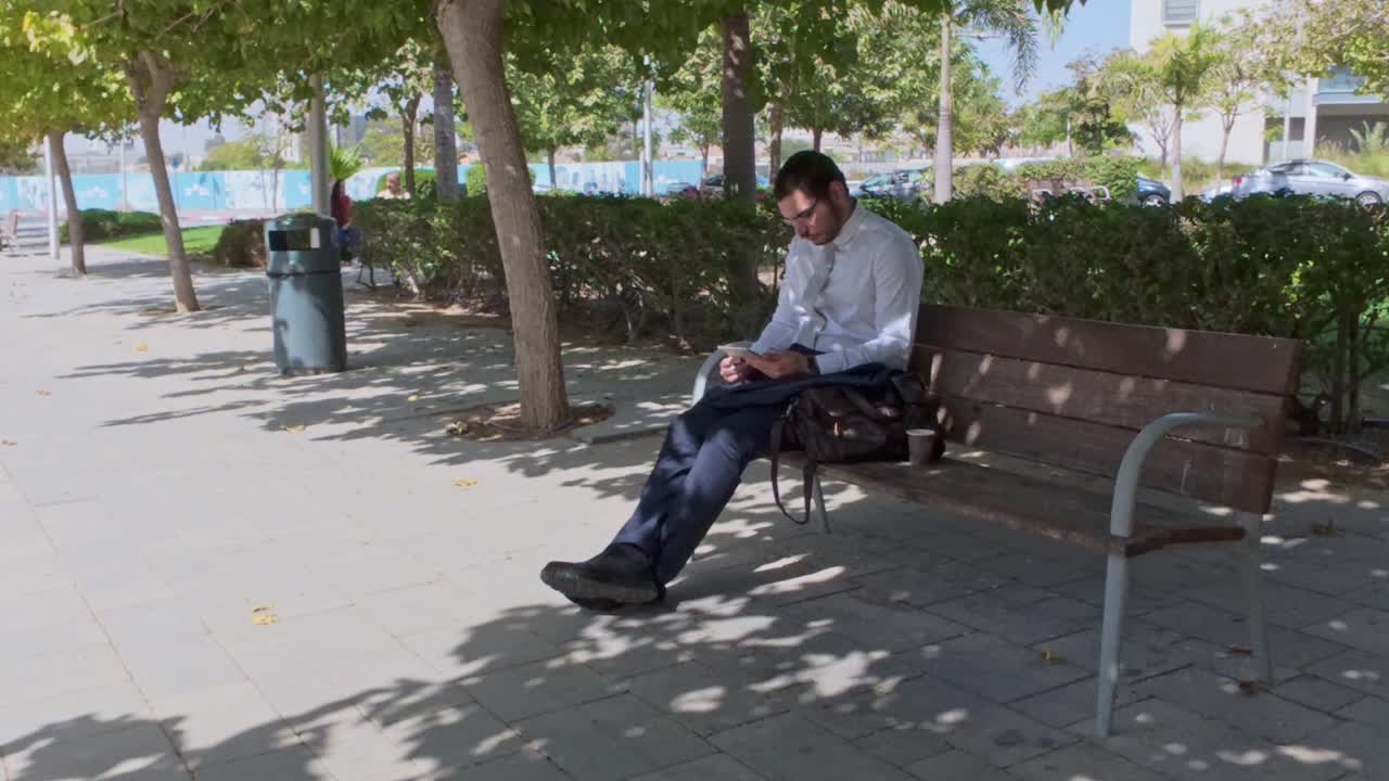 Uomo d'affari che lavora da remoto su una panchina in un parco ombreggiato.