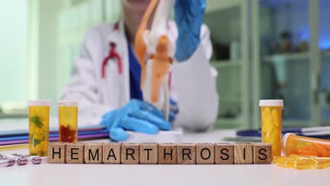 medical professional with knee model and pills, spelling "hemarthrosis" with blocks