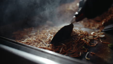 stirring around noodle dish on festival grill using metal spatulas