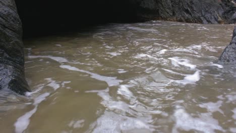 Close-up-of-small-waves-hitting-rocks-in-a-cave-near-the-beach