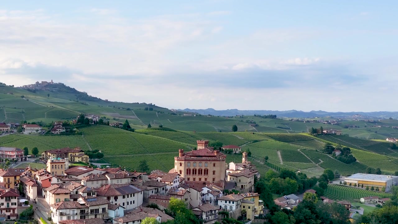 Ampia inquadratura paesaggistica di un villaggio storico italiano circondato da dolci colline verdi di vigneti.
