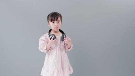 헤드폰을 끼고 있는 귀여운 아시아 소녀는 음악과 춤을 즐기며 스튜디오에서 행복하게 돌아다닙니다