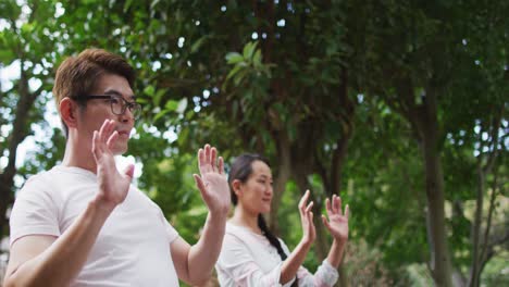 Happy-asian-couple-exercising-in-garden-with-daughter,-practicing-tai-chi-together