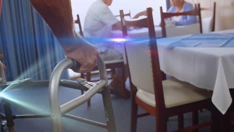 Animation-of-light-moving-over-senior-man-in-dining-room-using-walking-frame