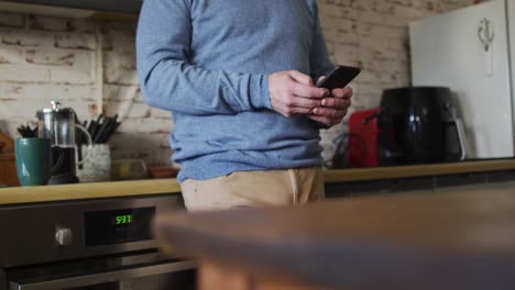 Sección-Media-Del-Hombre-Caucásico-Usando-Un-Teléfono-Inteligente-En-La-Cocina-De-Casa