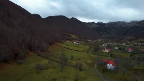 Alpine-village-in-Albania-with-green-meadow-and-houses-surrounded-by-leafless-trees-and-mouintains