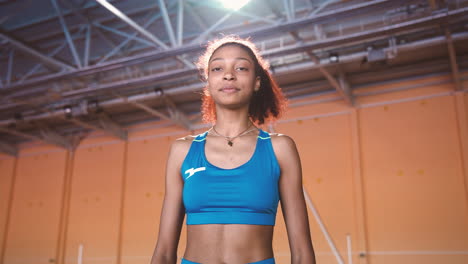 happy young sportswoman jumping and cheering while looking at camera in an indoor sport facility