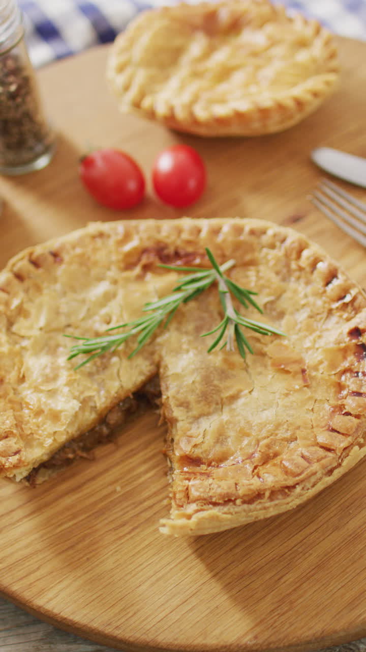 вертикальное видео выпеченных сочных пирогов, один недостающий кусочек и розмарин, с помидорами на столе.