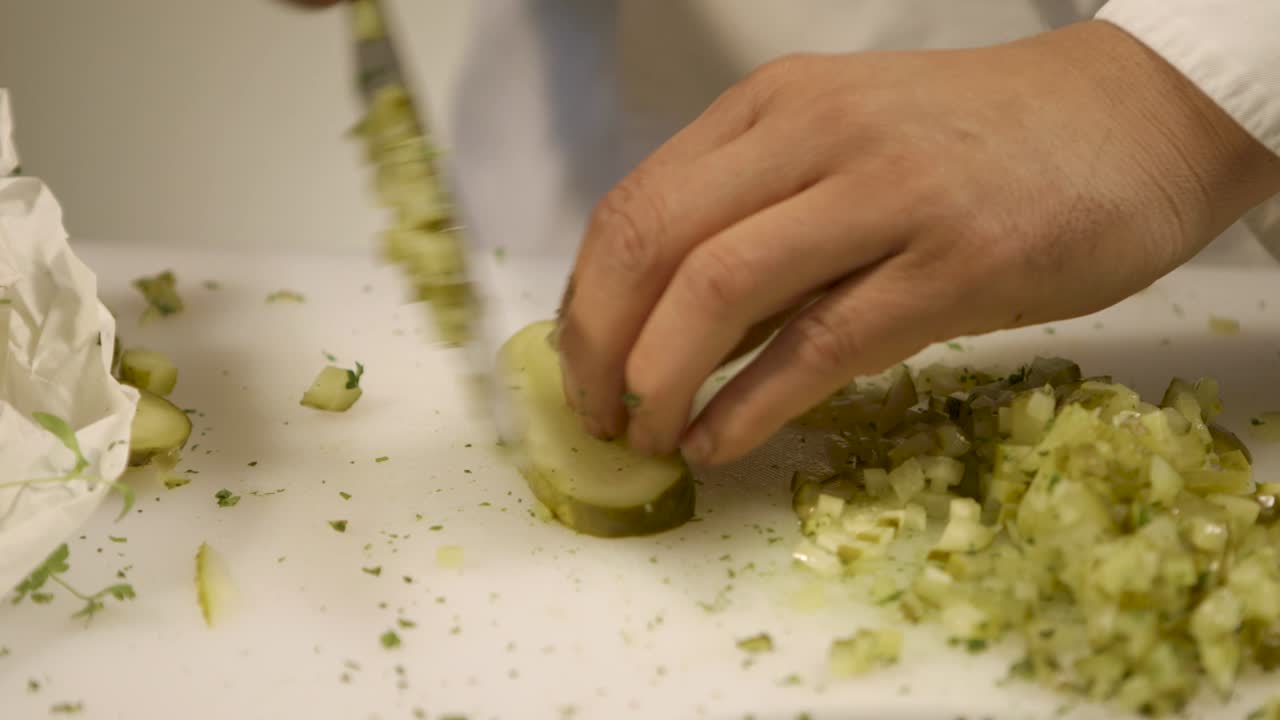 Close-up of hands chopping pickles on a white cutting board, kitchen preparation scene