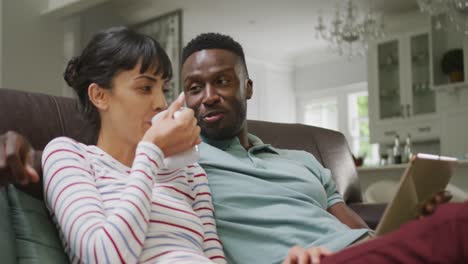 happy diverse couple sitting on couch and drinking coffee in living room