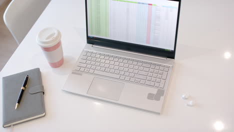 laptop displaying spreadsheet on screen, pen resting on notebook