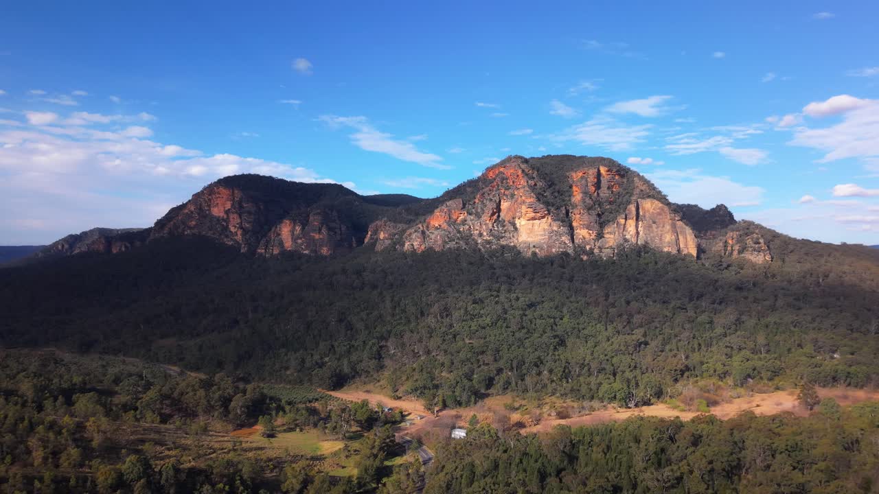 Midday light bathes cliff tops and treetops during dramatic drone pullback across Blue Mountains ridges, panoramic establish