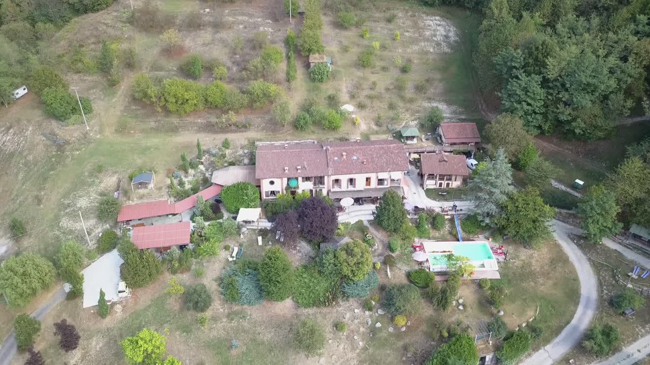 gran casa de vacaciones con una piscina y un camino en un bosque montañoso, vista aérea de drones en el campo italiano
