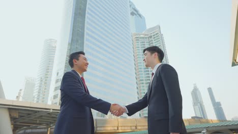 asian businessmen making handshake in the city building in the background. a partnership agreement is successful after complete the negotiation. business deal, merger and acquisition concepts.