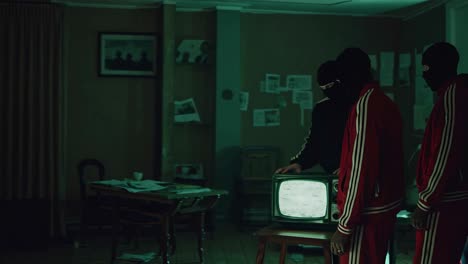 masked criminals inspecting a vintage tv in a dark room