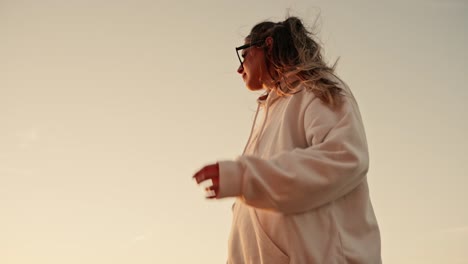 Toma-En-Cámara-Lenta-De-Una-Hermosa-Mujer-Arreglándose-El-Cabello-Mientras-Mira-Una-Puesta-De-Sol