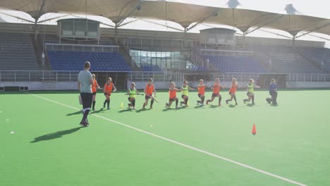 Coach-watching-female-hockey-players-exercising-on-the-field