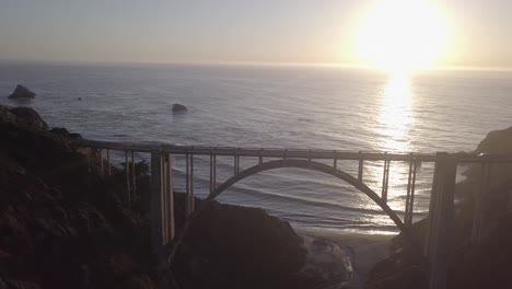 aerial drone shot of bixby bridge with sun and ocean behind