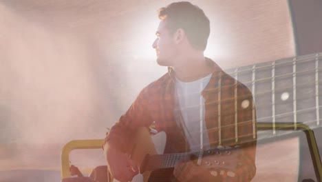 animación de luces sobre feliz hombre caucásico tocando la guitarra en la playa